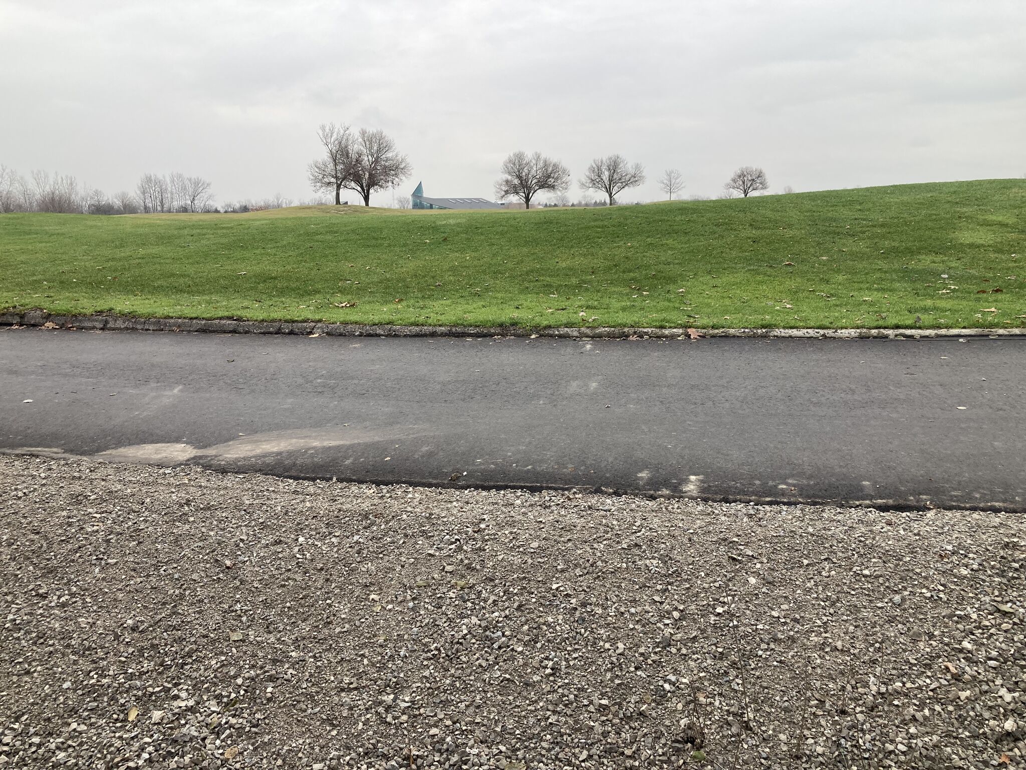 Freshly cleared and maintained golf course landscape with a paved path and gravel edge under an overcast sky.